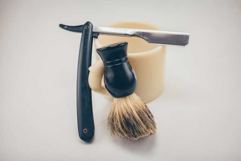 Straight razor, ceramic mug, and shaving brush arranged on a table for a classic wet shave